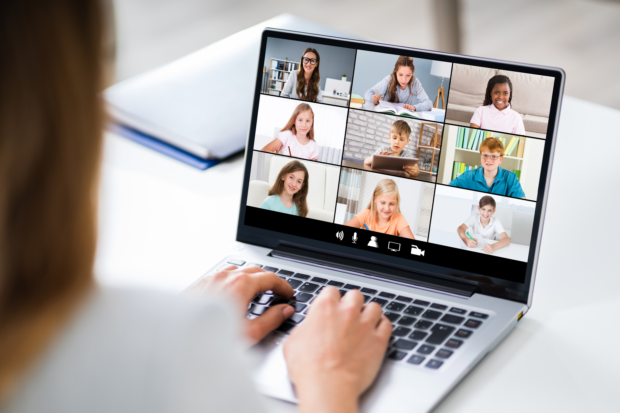 A teacher looking at a laptop screen while video chatting with a group of students