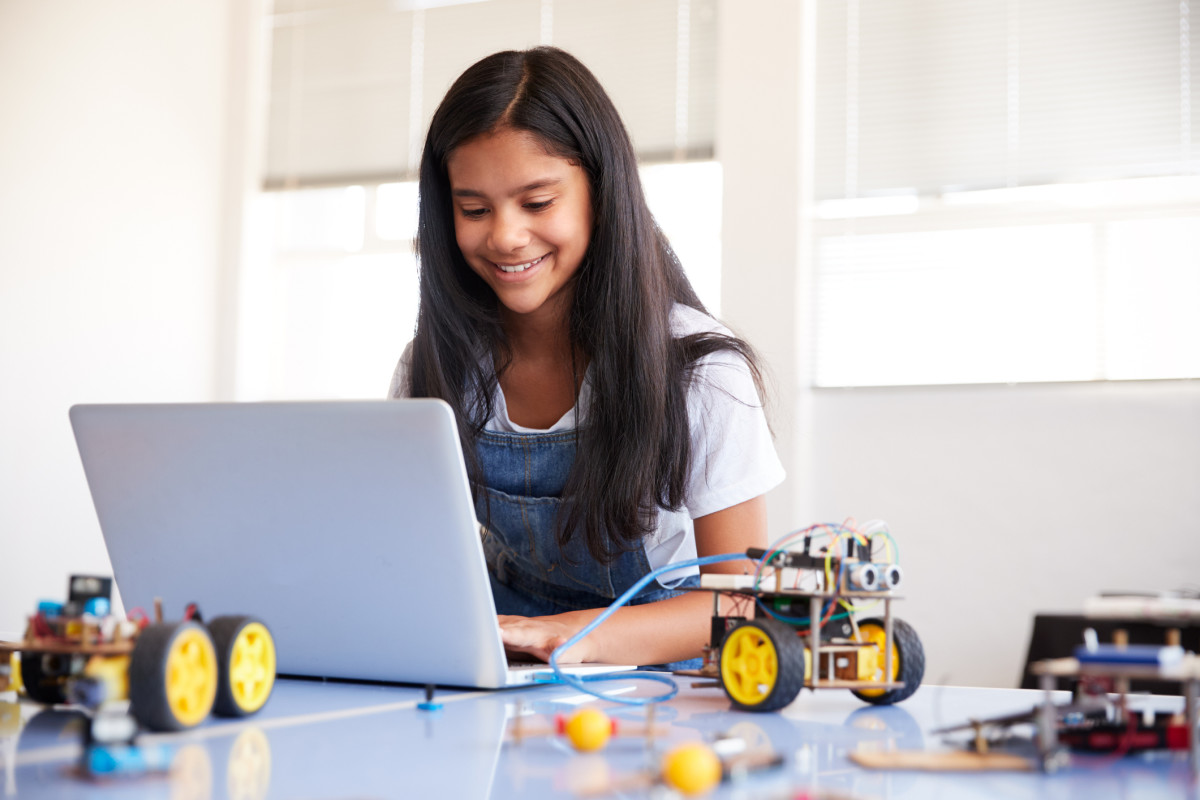 A young student works at a table on a laptop, assembling a model car