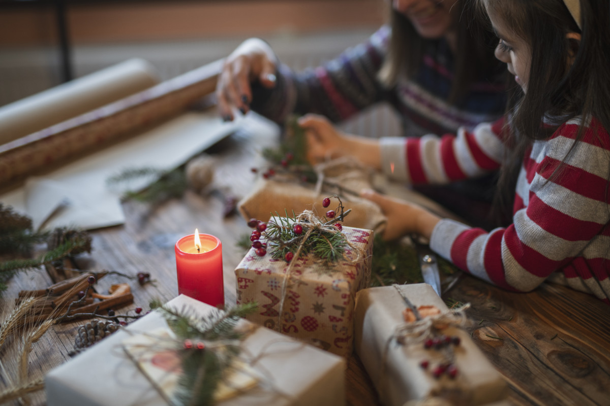 A parent and child wrap gifts near a candle