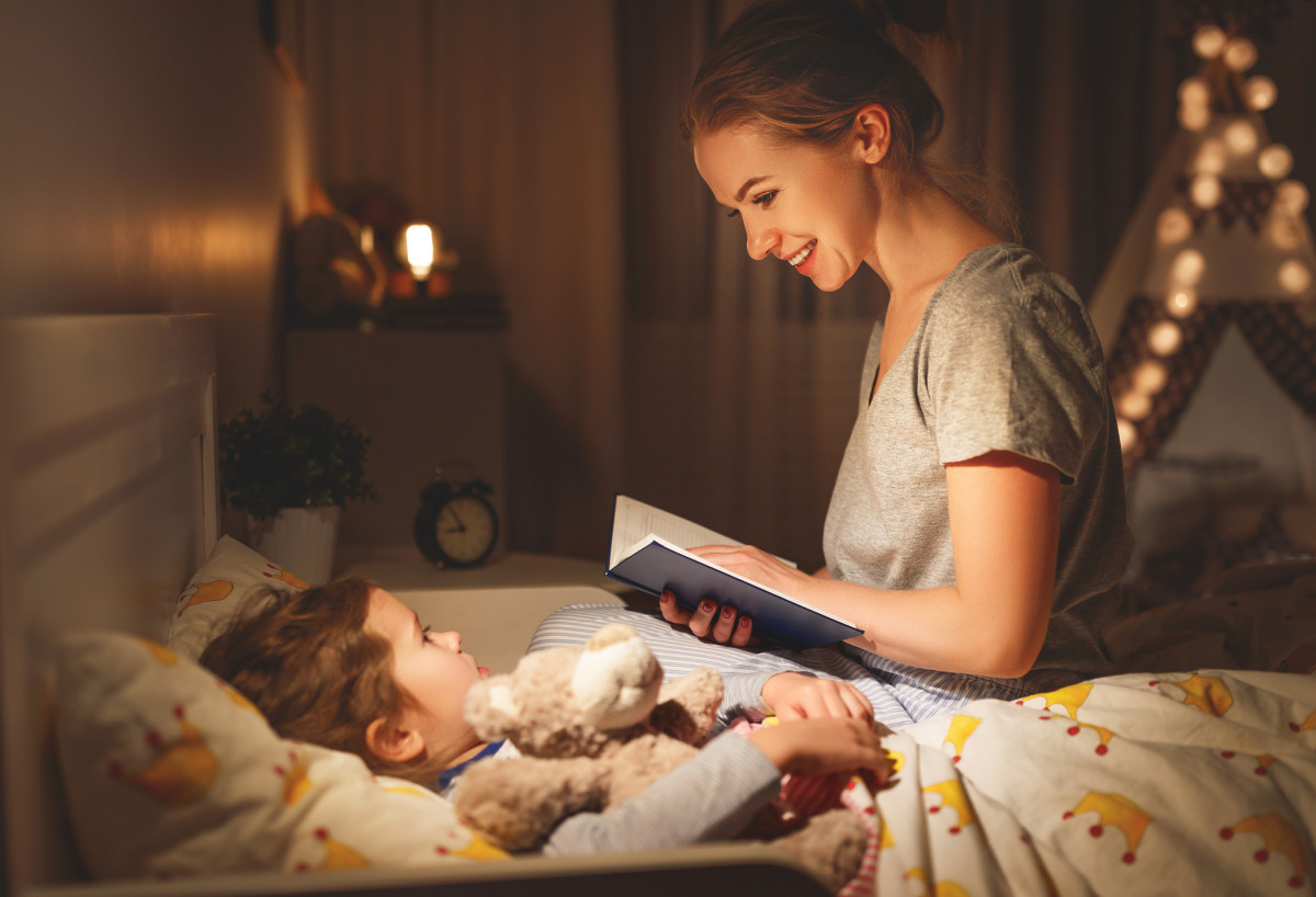 A mother reads to her child who is laying in bed