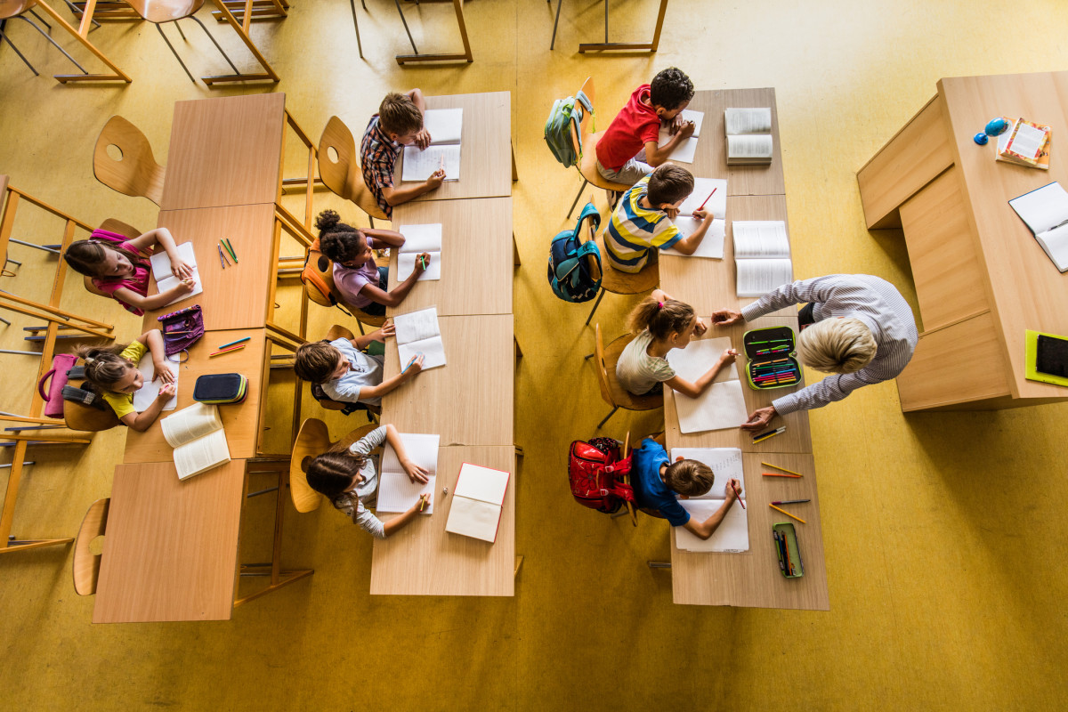 An image of a teacher working with students as they write in notebooks