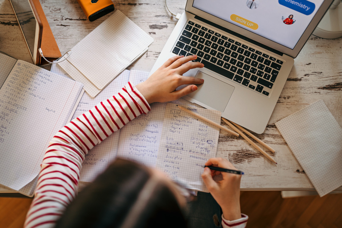 A student works on homework with papers spread around them and a laptop open