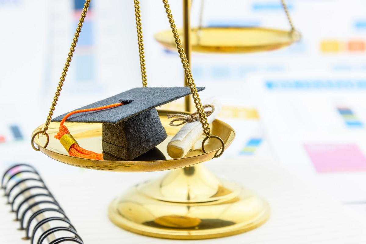 A brass scale holds a mortar board and diploma on one of the scales