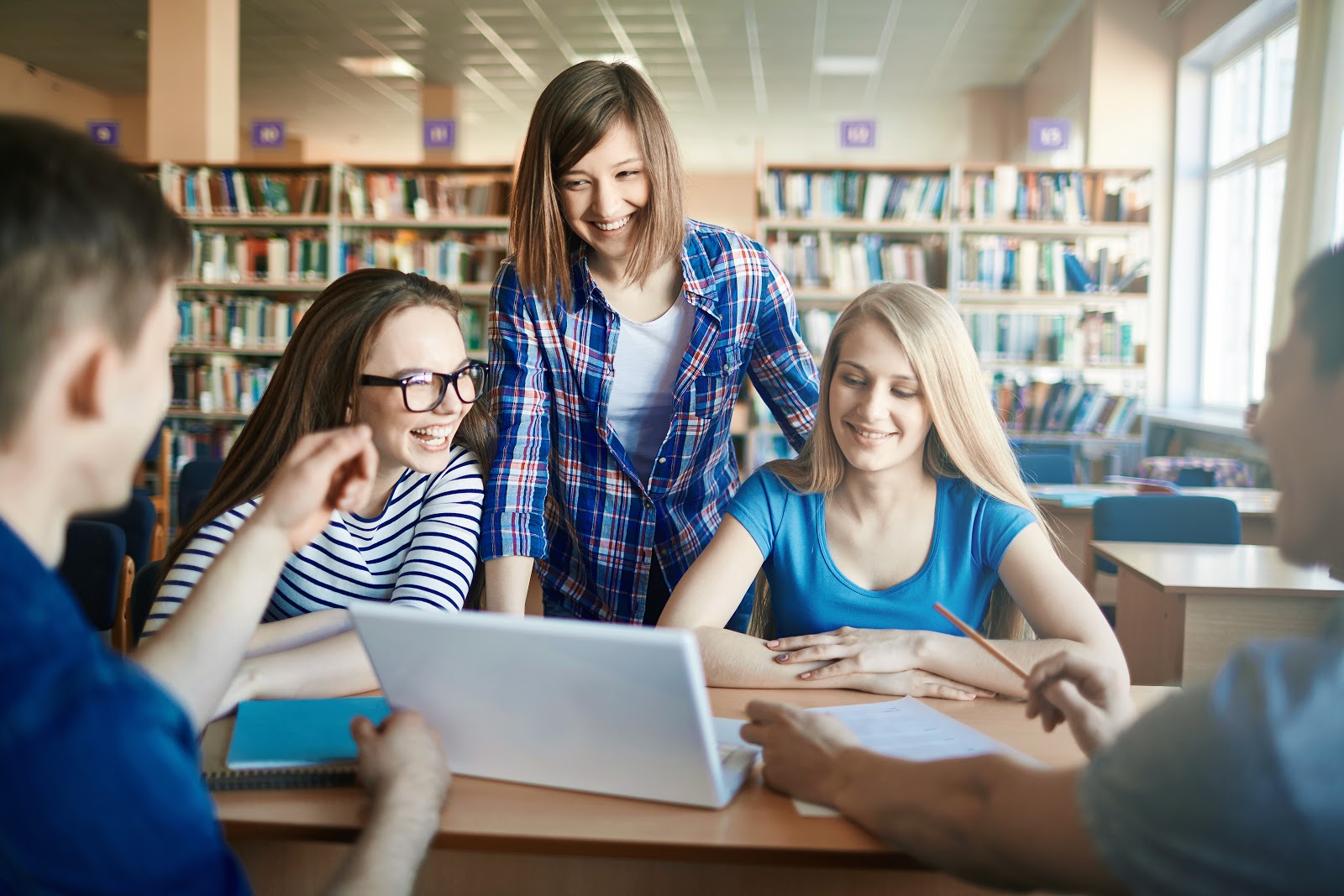 A teacher works with a group of students on their laptops in the library