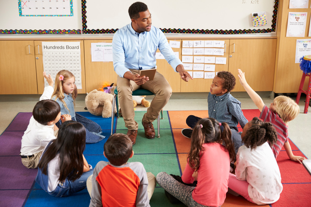 Photo of a teacher surrounded by a circle of students sitting on the floor and smiling