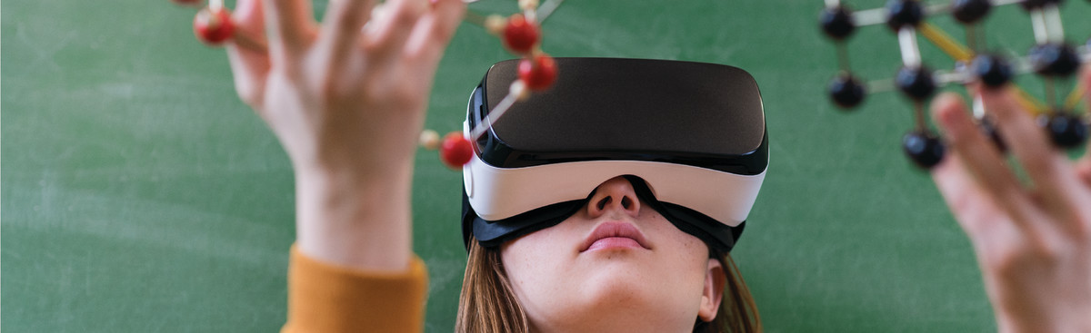 A student touches a model of a molecule while wearing a VR headset