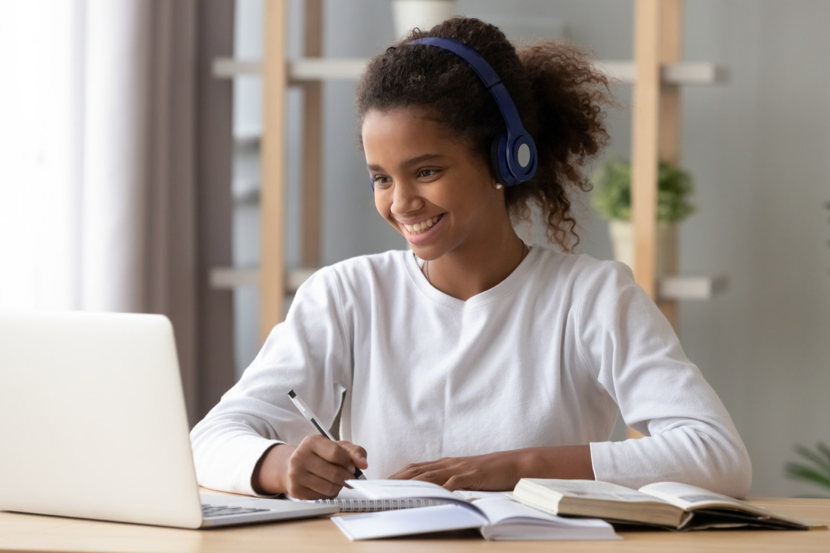 Photo of a girl wearing headphones and smiling as she works at her computer