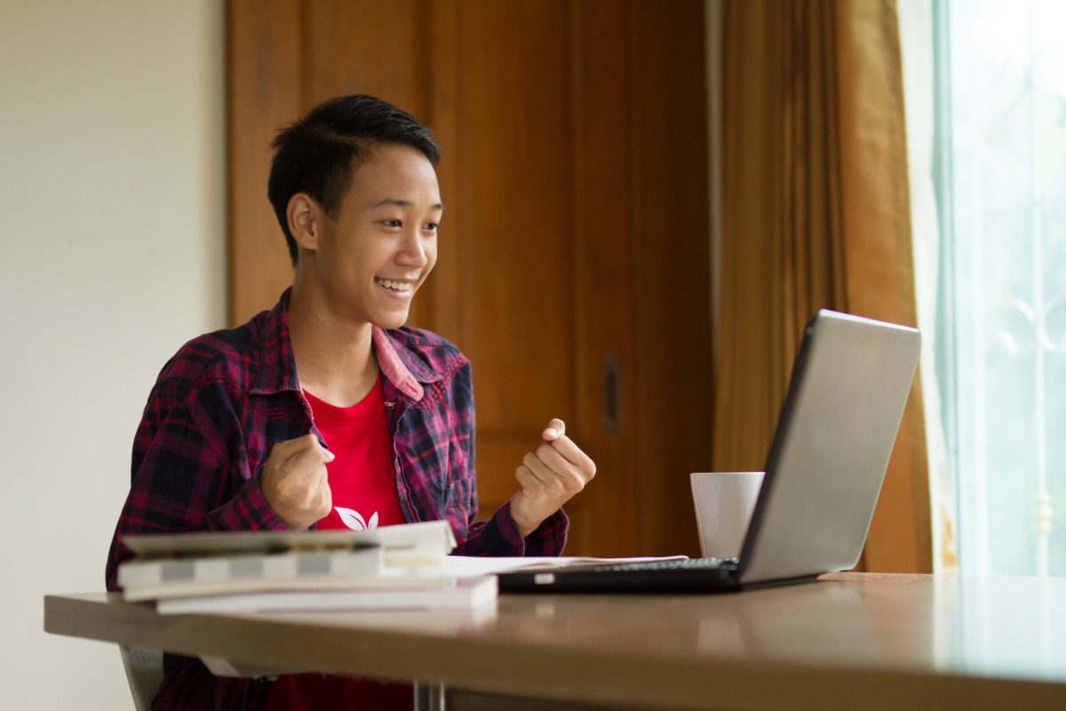 A student looks happily at a laptop screen