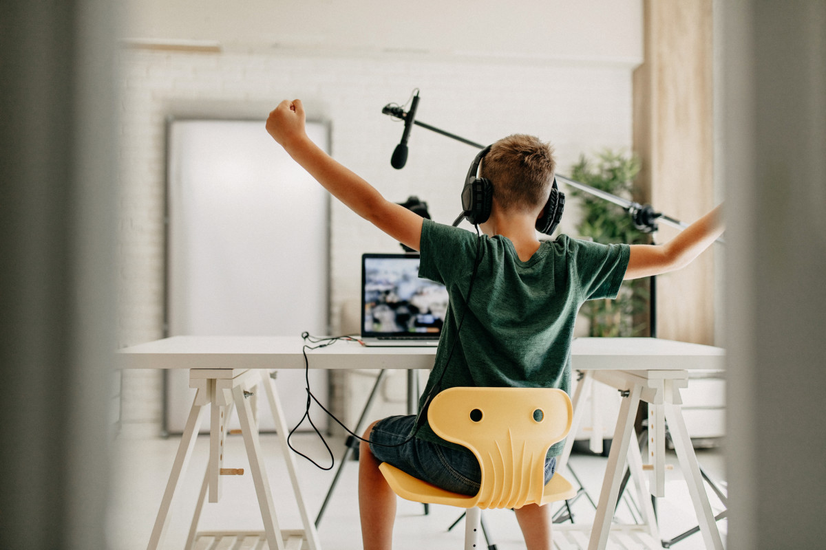 Student happy working on a computer at home with headphones and a microphone