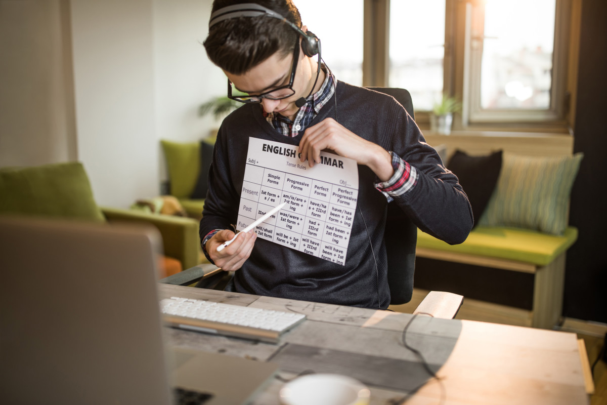 A teacher points to a piece of paper in front of a laptop screen