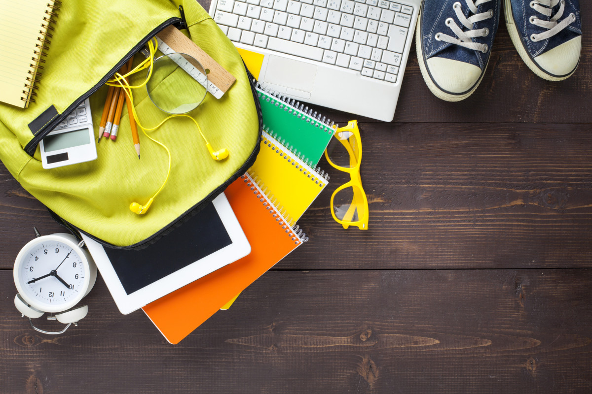 An alarm clock, backpack with school supplies, laptop, and shoes on a wooden floor