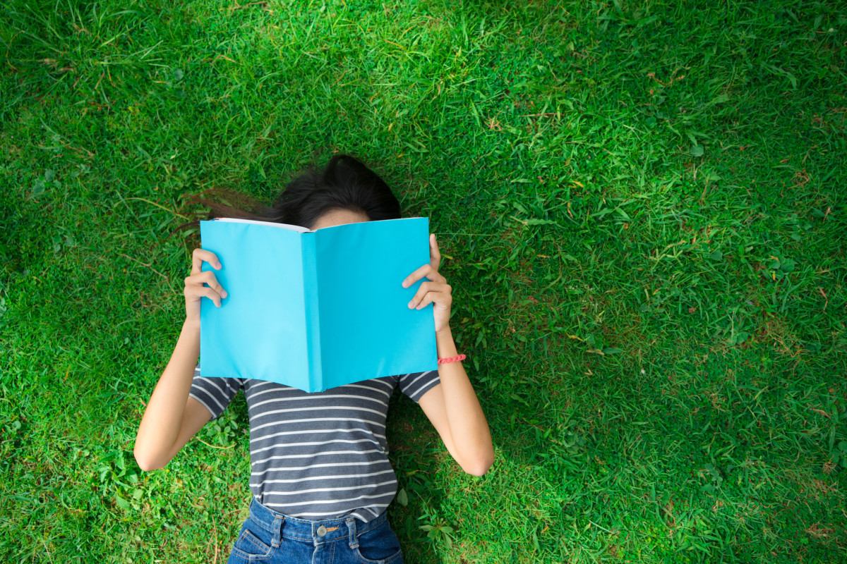 Student reading a book on a green lawn