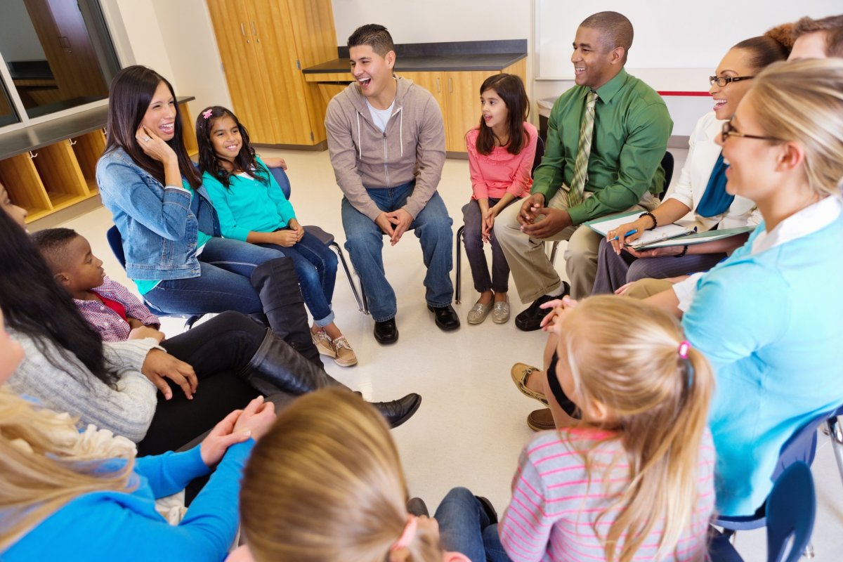 Students and Parents sitting in a circle in a classroom smiling and talking