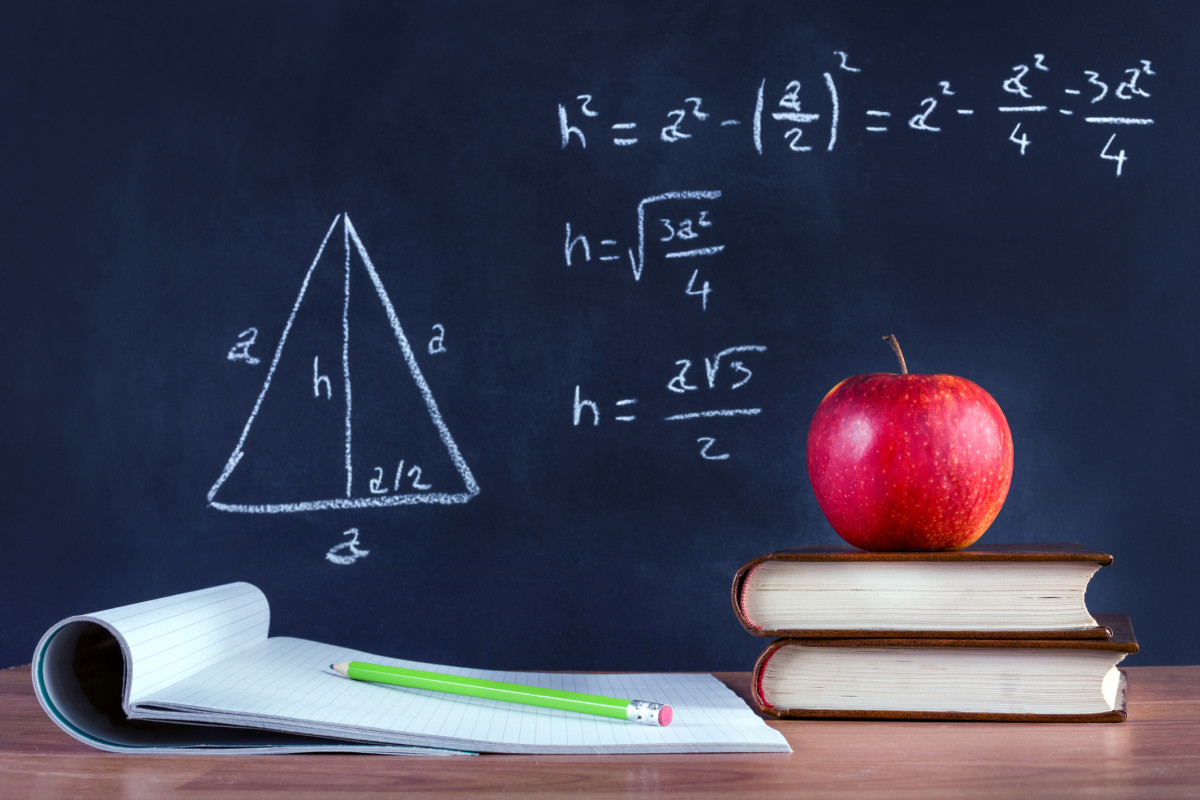 A notebook with a stack of books and an apple sit in front of a blackboard with a math problem written on it