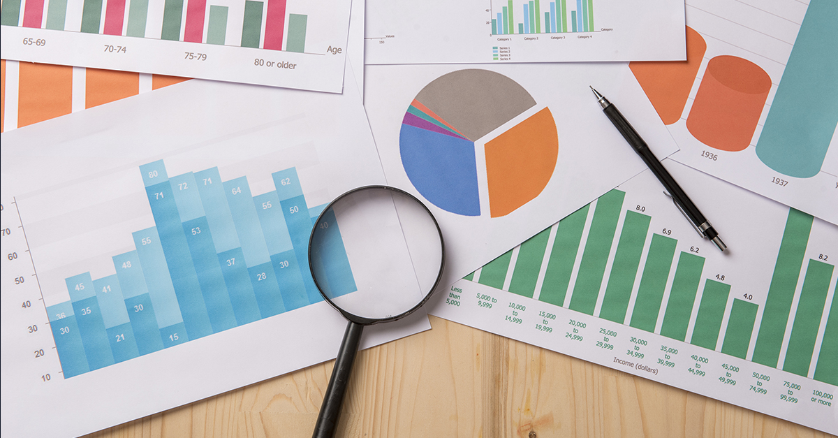 A stack of printed graphs and charts on a table with a magnifying glass and a pencil