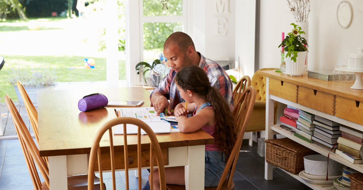 A caregiver sits at the dining room table with a student going over homework