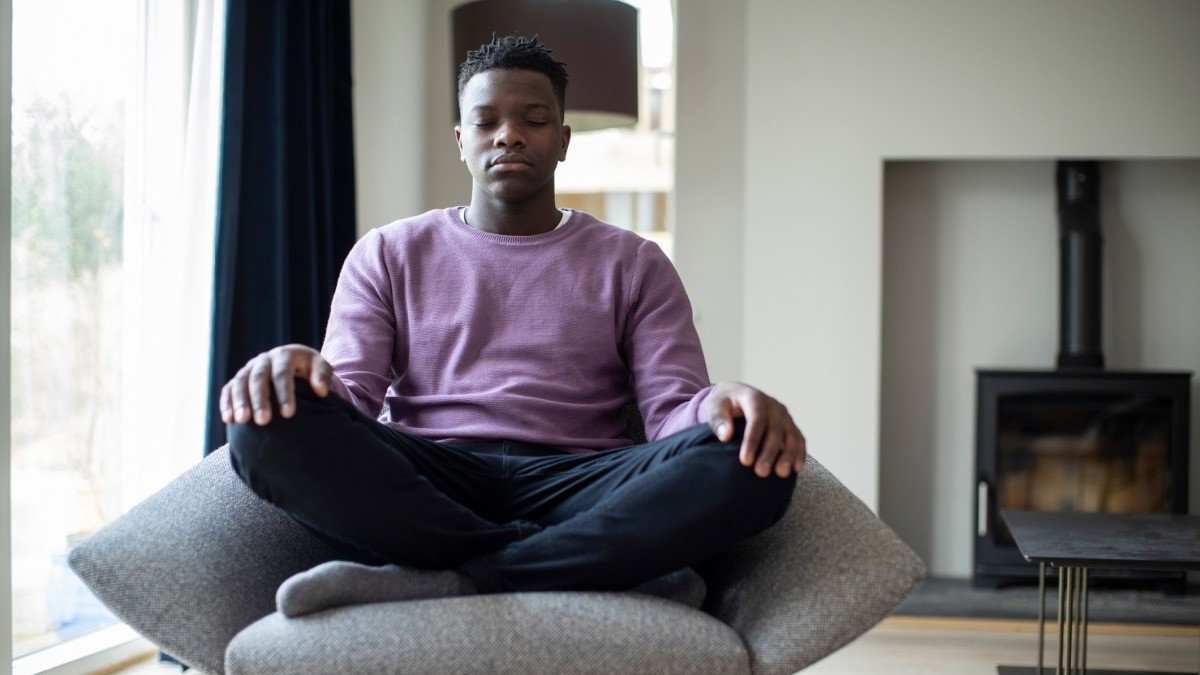 A man sitting on a chair with his legs crossed and his eyes closed in a meditative pose