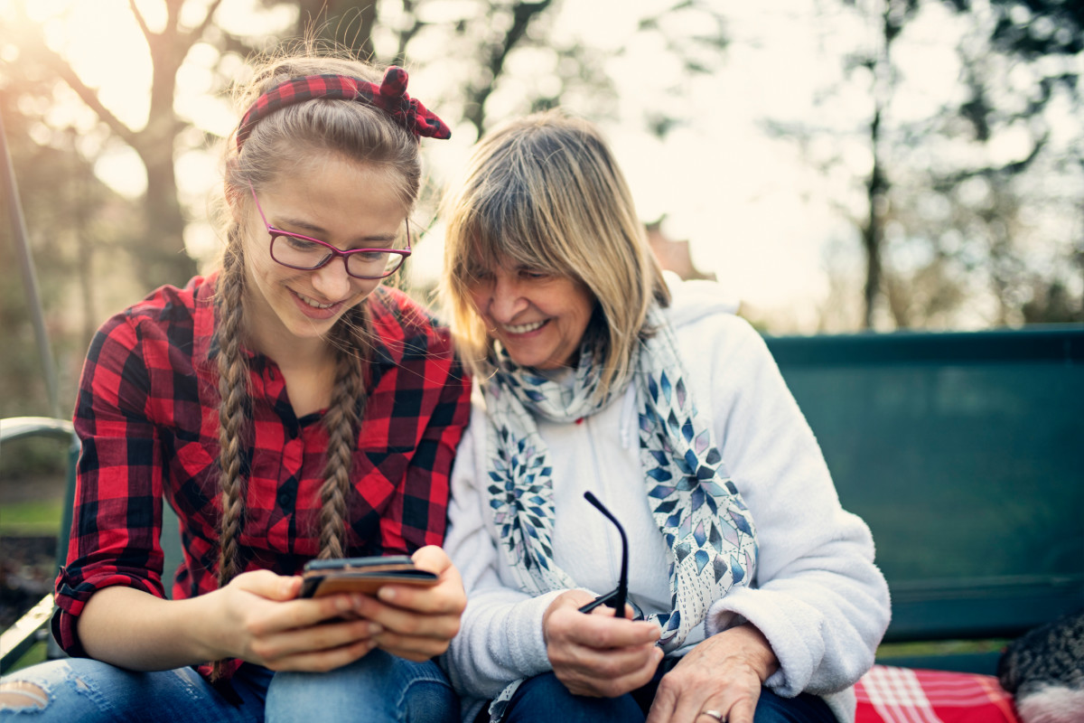 A young girl showing an older woman something on her phone and both are smiling and enjoying the moment