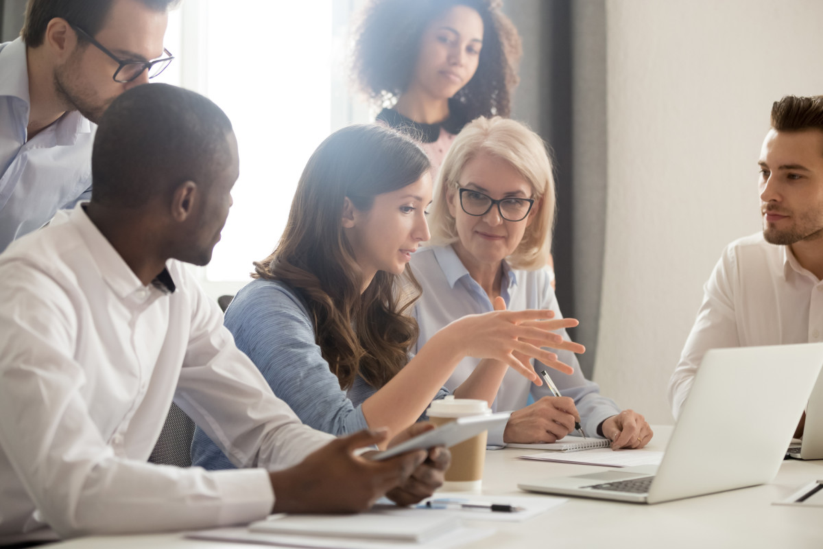 A group of adults gathered around a woman leading a discussion while working on a computer