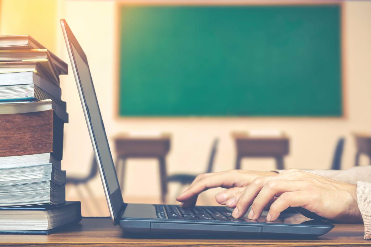 A person typing on a laptop next to a stack of books