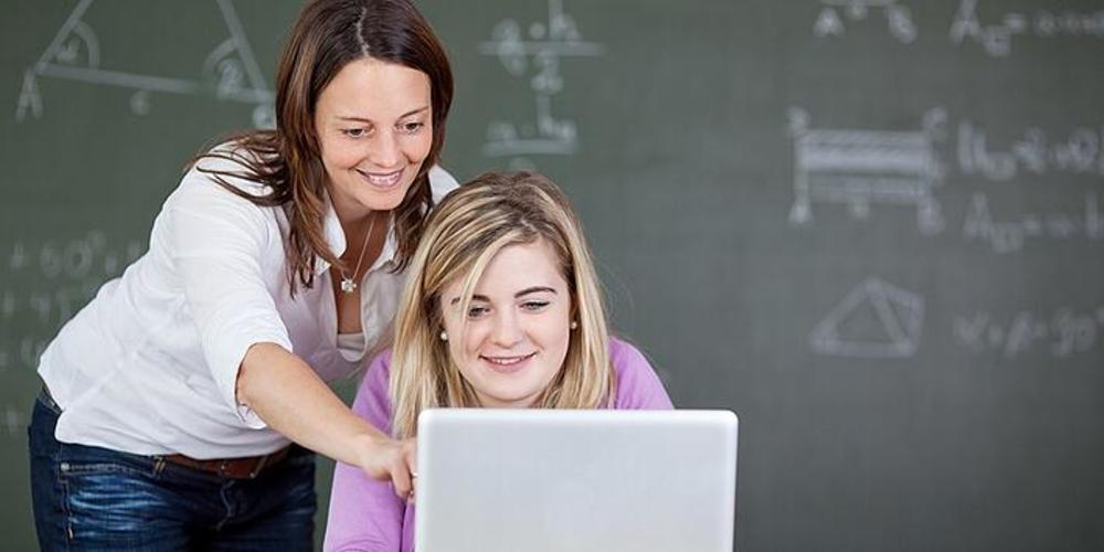 Teacher and student smiling and working on a computer in a classroom