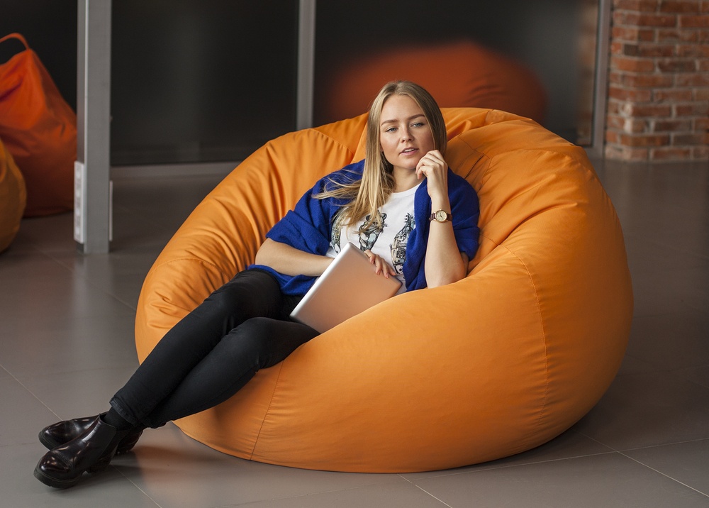 A woman sits in an orange bean bag chair holding a tablet