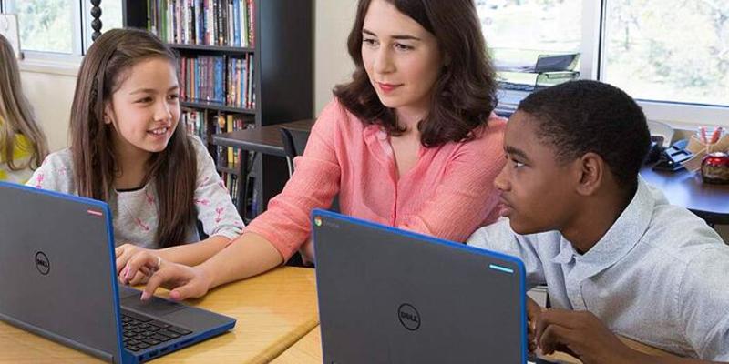 A teacher works with two students on their laptops