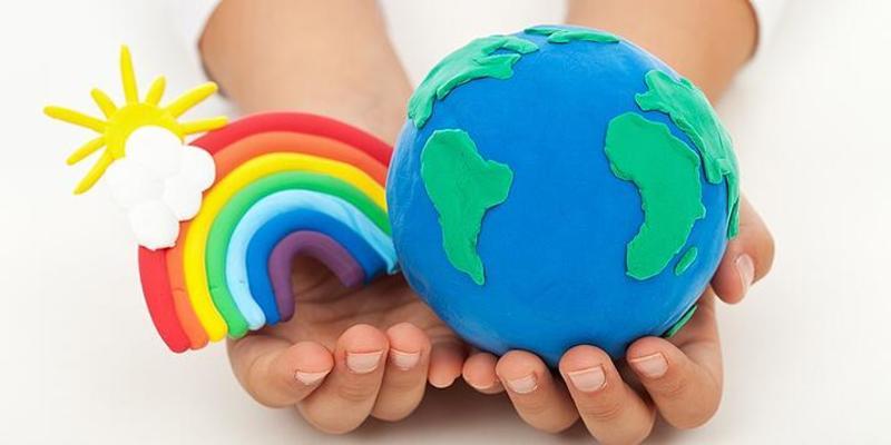 A person holds clay models of the earth and a rainbow with a cloud and a sun