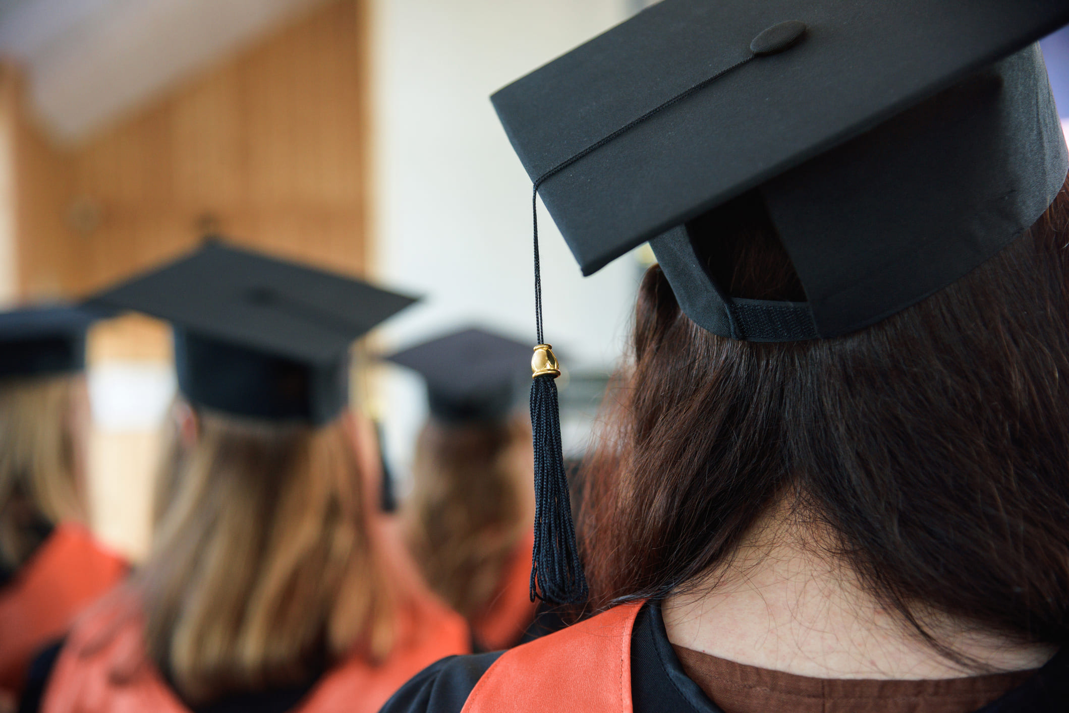 Students wearing graduation caps and gowns face away from the camera