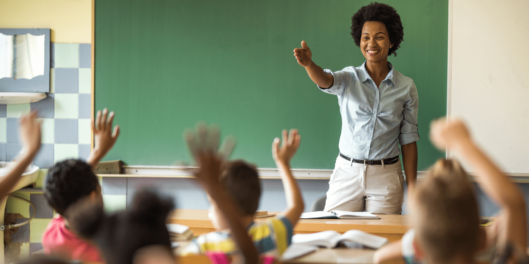 Photo of a teacher leading a class with students raising their hands