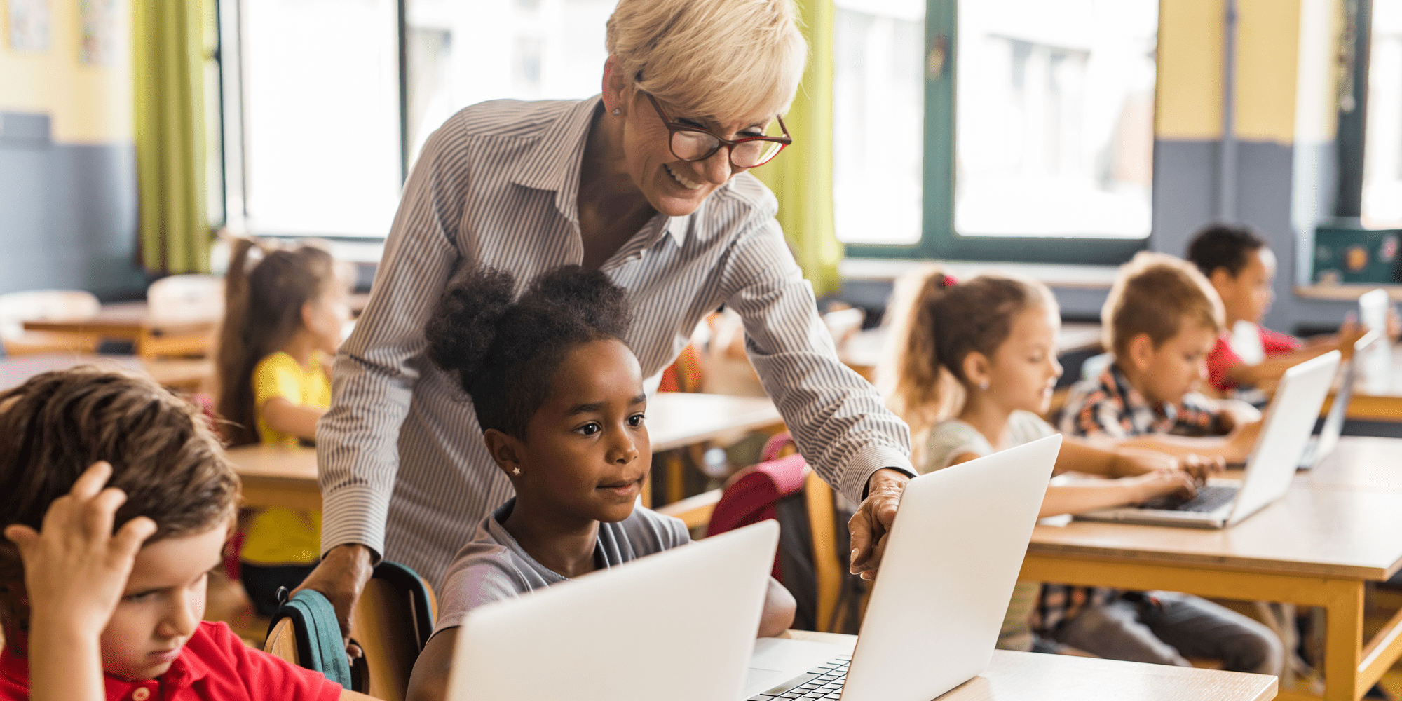 Teacher smiling and working with students on computers